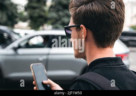 A young man in sunglasses uses a smartphone, close-up. Stock Photo