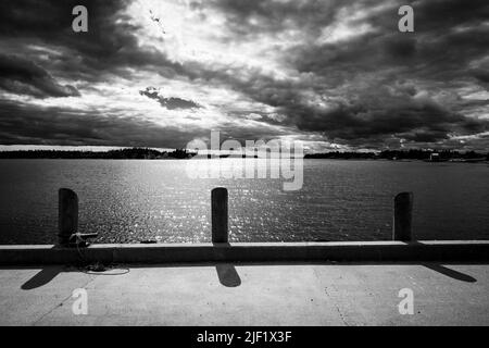 Black and white image of sun breaking through clouds taken from a wharf. Stock Photo