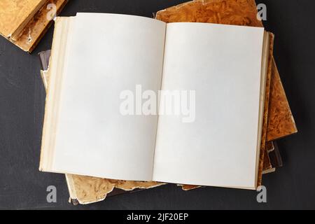 Open vintage book or notebook in a dust jacket on a stack of old shabby books on a dark concrete table Stock Photo