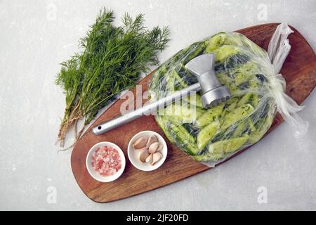 Appetizer Broken salted cucumbers in a plastic bag on a wooden cutting board with a kitchen chop hammer Stock Photo