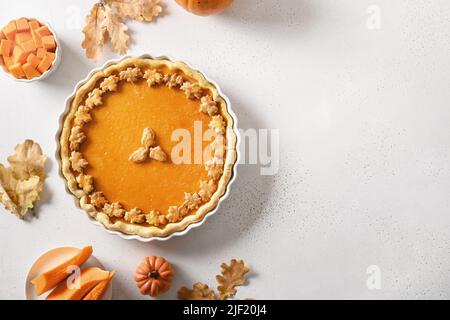 Thanksgiving Day American Pumpkin Pie decorated autumn leaves on white background. View from above. Flat lay. Copy space. Stock Photo