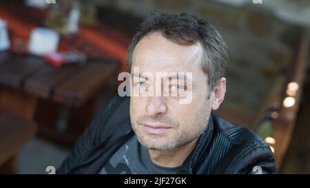 Cute smiling middle-aged handsome man standing outdoors. Portrait of smiling man looking at camera on background of spring tree in daylight. Stock Photo