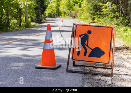 Close up view of a warning, beware of workforce in road sign and traffic cone on a highway. Blurry rural freeway and cones are seen in background. Stock Photo