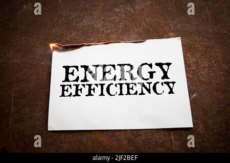 ENERGY EFFICIENCY. Burning paper with text on a rusty metal background. Stock Photo
