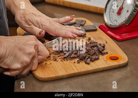 Chef cuts bitter chocolate into pieces on wooden board in the kitchen. Stock Photo