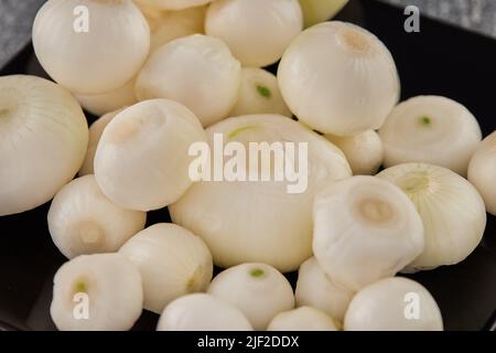 Shallots on black plate are peeled and ready to cook Stock Photo