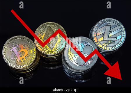 Cryptocurrency tokens, including Bitcoin, Ethererum Ripple, and Litecoin saw from above on a black background. A red arrow goes down, representing the decline in the exchange rate of the coins.  Stock Photo