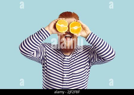 Funny man holding halves of citrus juicy fruits and them closing his eyes on light blue background. Stock Photo