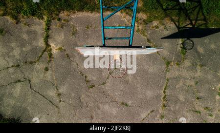 Old basketball backboard. Made from boards. Peeling paint and a battered basket. There is an old cracked asphalt on the site. Shot from above. Aerial Stock Photo
