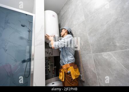 Plumber installing electric heating boiler. Young handyman in uniform setting up electric heating boiler at home Stock Photo