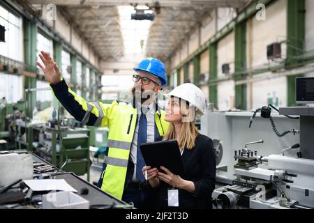 Male and female industrial engineers discussing factory's new machinery project and using tablet. Stock Photo