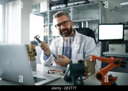 Robotics engineer working on desing of modern robotic arm and sitting at desk in laboratory. Stock Photo