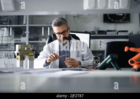 Robotics engineer working on desing of modern robotic arm and sitting at desk in laboratory. Stock Photo