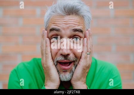 Mature man with shocked, amazed expression touching his face on street background. Stock Photo