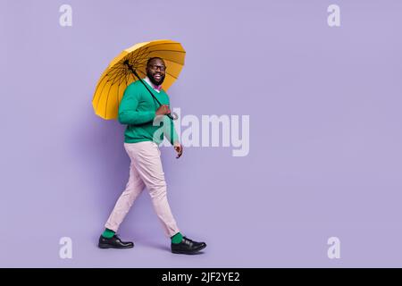 Full size profile portrait of positive nice person hold umbrella walking isolated on purple color background Stock Photo