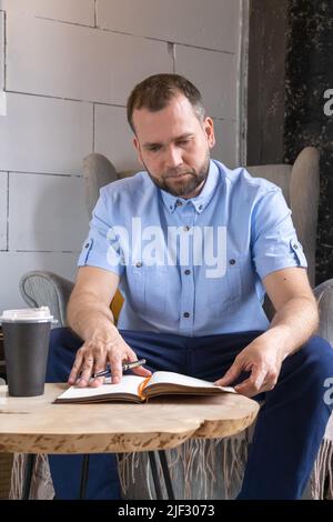 Focused middle aged 40s businessman writing notes in personal diary, planning work day, checking timetable or writing important information by hand in Stock Photo