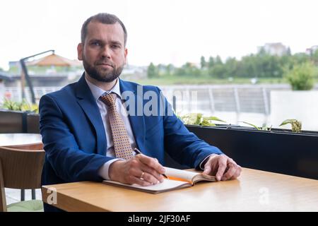 Focused middle aged 40s businessman writes notes in a personal diary, plans a working day, checks a schedule, or writes important information by hand Stock Photo