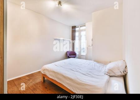 Comfortable bed with ornamental blanket placed near glass door and wardrobe in light bedroom Stock Photo