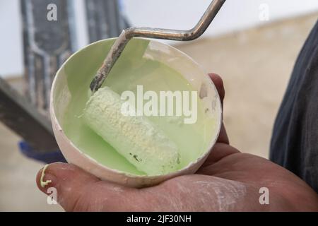 Craftsman's hand holding a roller in a can of green paint. Painter painting a wall with paint roller. Repair by myself. DIY concept Stock Photo