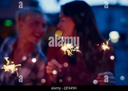Two happy women blurred playing with fireworks on holiday together. Cheerful friends blurred celebrating playing with fireworks at night during Stock Photo