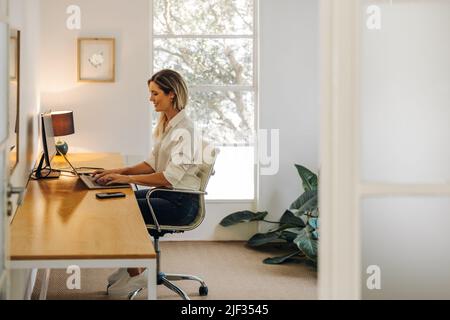 Happy young businesswoman smiling while typing on a laptop keyboard in her office. Cheerful young businesswoman consulting her business clients online Stock Photo