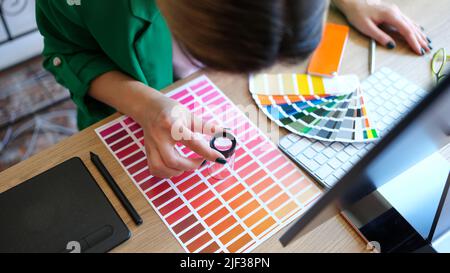 Woman chooses through magnifying glass color and shades on color palette Stock Photo