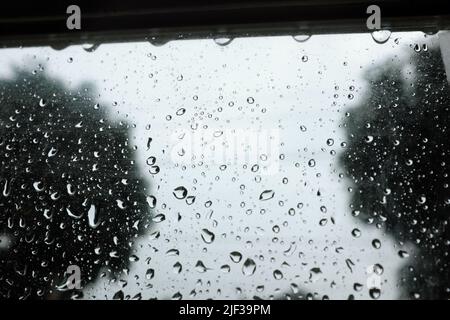 Selective focus of rain water droplets on house glass window. Rainy season background. Stock Photo