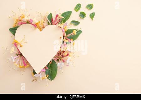 Heart made from lonicera periclymenum belgica flowers and beige paper cut. Stock Photo