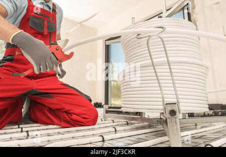 Caucasian HVAC Worker with Tube Slicer in His Hand Cutting Radiant Floor Heating Plastic Pipeline. Heating and Cooling Industry Theme. Stock Photo