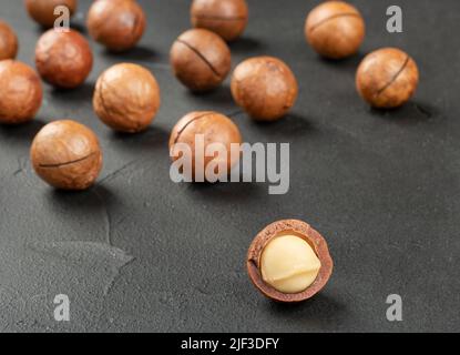 Scattered macadamia nuts in their shells on a dark concrete background Stock Photo
