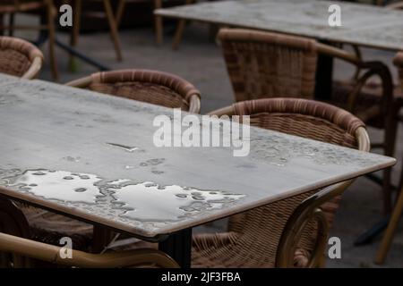 Empty table and empty chairs of summer restaurant or beer garden in summer on rainy day with raindrops and no guests, no income on sidewalk seating Stock Photo