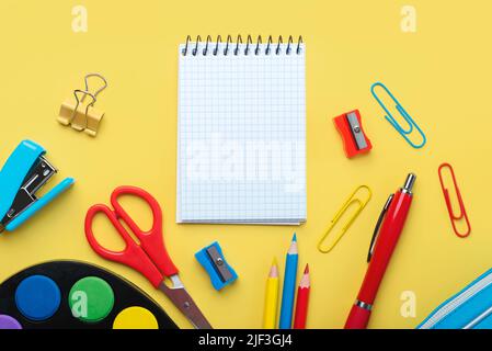 Top view of blank spiral notepad and school supplies with space for text on yellow background. Back to school concept Stock Photo