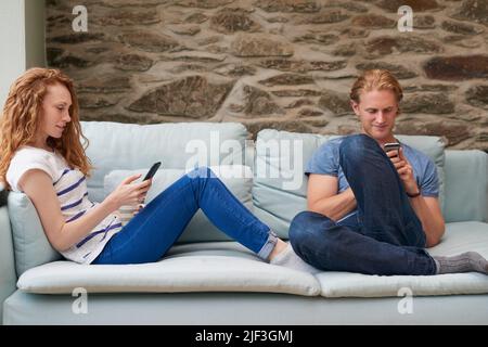 A young couple using smartphones while spending time together at home Stock Photo