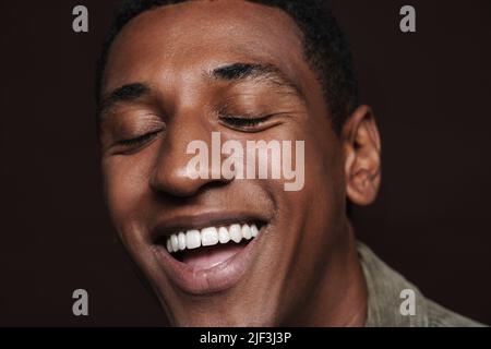 Young black man laughing with his eyes closed isolated over brown wall Stock Photo