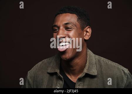 Young black man dressed in shirt laughing while showing his tongue isolated over brown wall Stock Photo