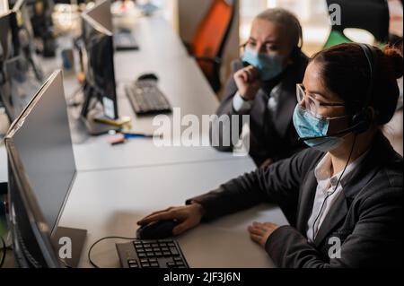 Two women in medical masks and headsets are working in the office Stock Photo