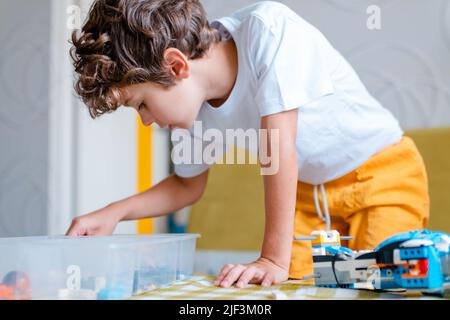 Kid collects robot from plastics details and programmed on tablet, robotics. Stock Photo