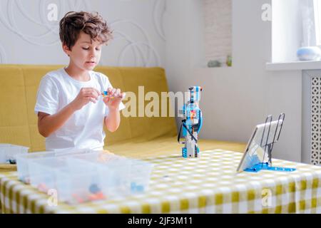Kid collects robot from plastics details and programmed on tablet, robotics. Stock Photo