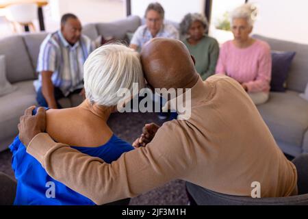Rear view of multiracial senior man embracing woman in group therapy session at nursing home Stock Photo