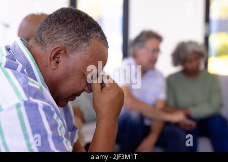 Close-up of depressed caucasian senior man with head in hand sitting with multiracial friends Stock Photo