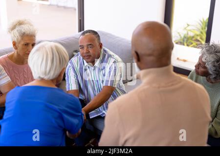 Multiracial seniors looking at friends holding hands and comforting in group therapy session Stock Photo