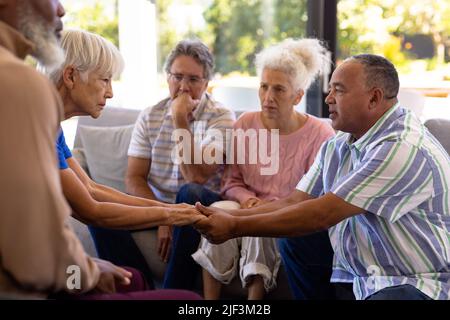 Multiracial seniors holding hands and comforting while sitting with friends in group therapy session Stock Photo