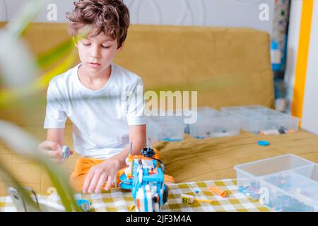 Kid collects robot from plastics details and programmed on tablet, robotics. Stock Photo