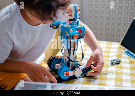 Kid collects robot from plastics details and programmed on tablet, robotics. Stock Photo