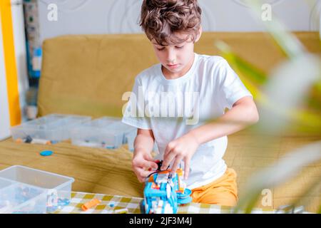 Kid collects robot from plastics details and programmed on tablet, robotics. Stock Photo