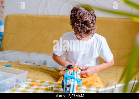 Kid collects robot from plastics details and programmed on tablet, robotics. Stock Photo