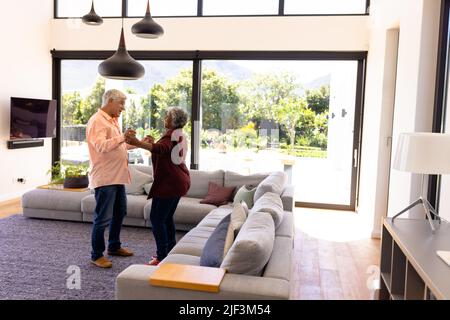 Happy multiracial senior friends holding hands and dancing by sofa in nursing home Stock Photo