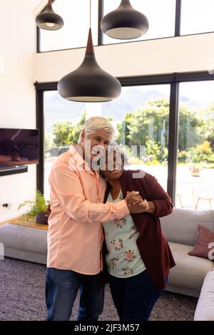 Portrait of cheerful multiracial senior friends embracing and dancing against window in nursing home Stock Photo