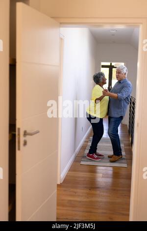 Cheerful multiracial senior friends dancing in corridor at nursing home seen through doorway Stock Photo