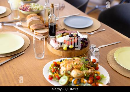 High angle view of chicken with cherry tomatoes, cheese, bread and grapes served on dining table Stock Photo